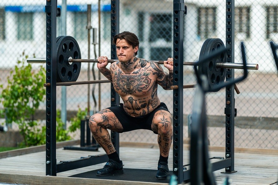 Mies treenaa ulkona kyykkj� levytangolla.