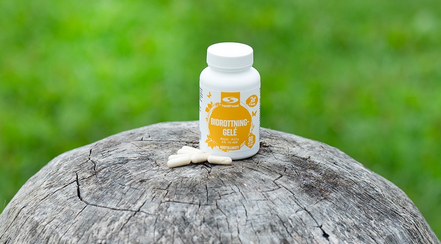 Healthwell Mehil�iskuningatargeeli -purkki ja muutama kapseli puisen p�lkyn p��ll�, taustalla nurmikkoa.