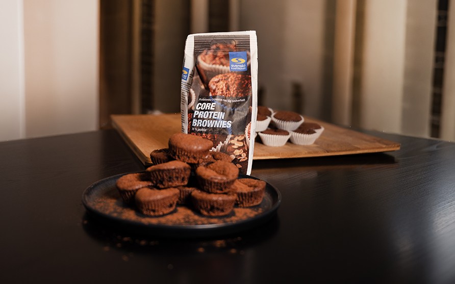 Keski�ss� p�yd�ll� Core Protein Brownies -leivontaseospussi, edess� mustalla lautasella valmiita browniemuffineja kuin my�s taustalla puisella tarjottimella.