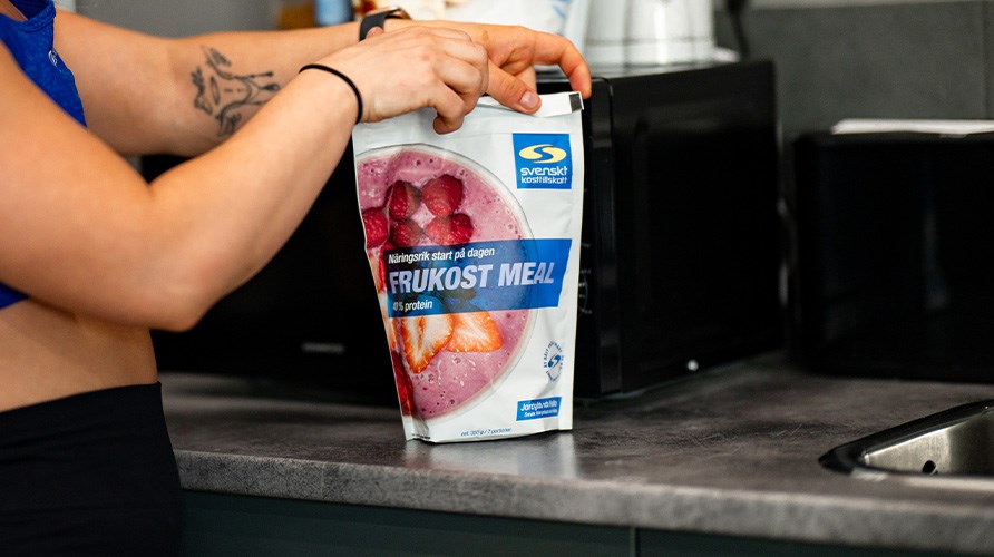 Treenivaatteissa oleva nainen pit�� kiinni Core Frukost Meal -pussista, joka on keitti�tason p��ll� mikron edess�.