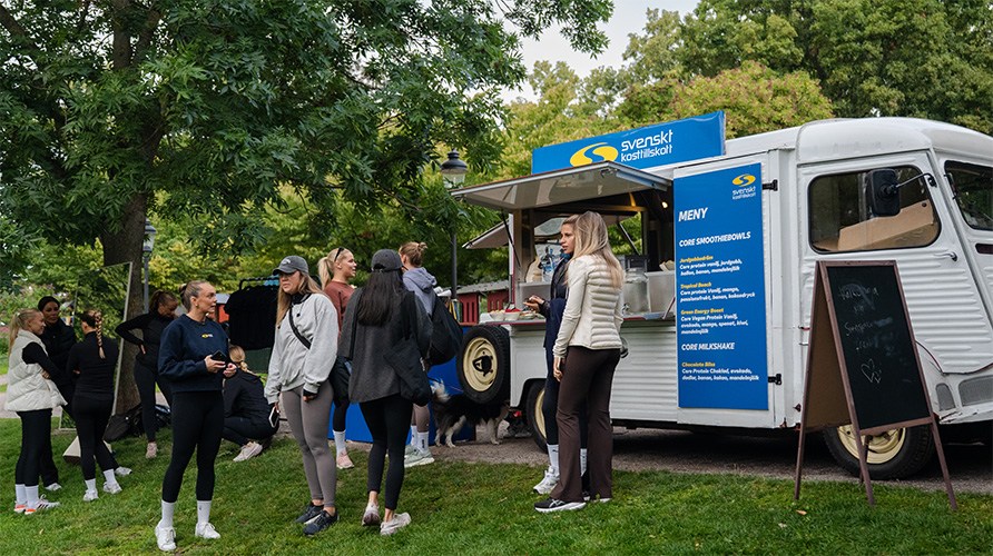 Ett event d�r en grupp m�nniskor st�r p� en gr�smatta bredvid en foodtruck som �r m�rkt med Svenskt Kosttillskotts logotyp. 