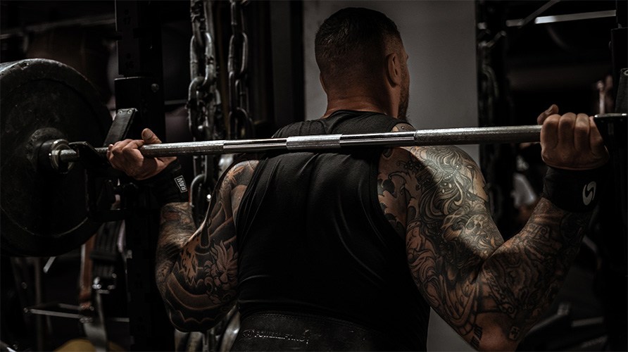 Mies, jolla on lihaksikas selk�, seisoo painotangon ��rell�.